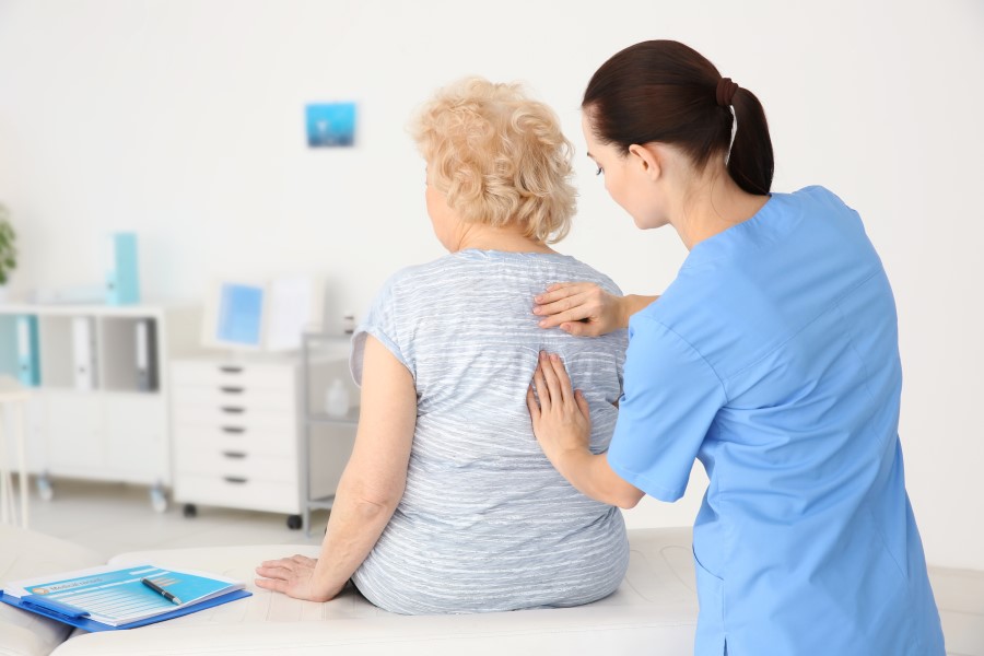 Starsza kobieta ma badany kręgosłup przez lekarkę.