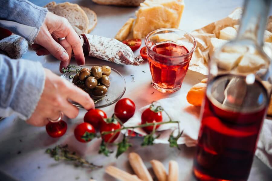 Kobieta sięga po jedzenie, obok stoi szklanka oraz butelka z alkoholem.