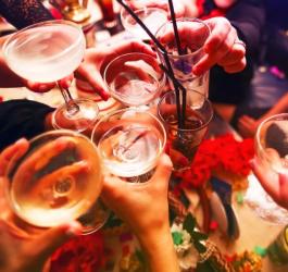 Grupa znajomych wznosi toast kieliszkami i szklankami z alkoholem.