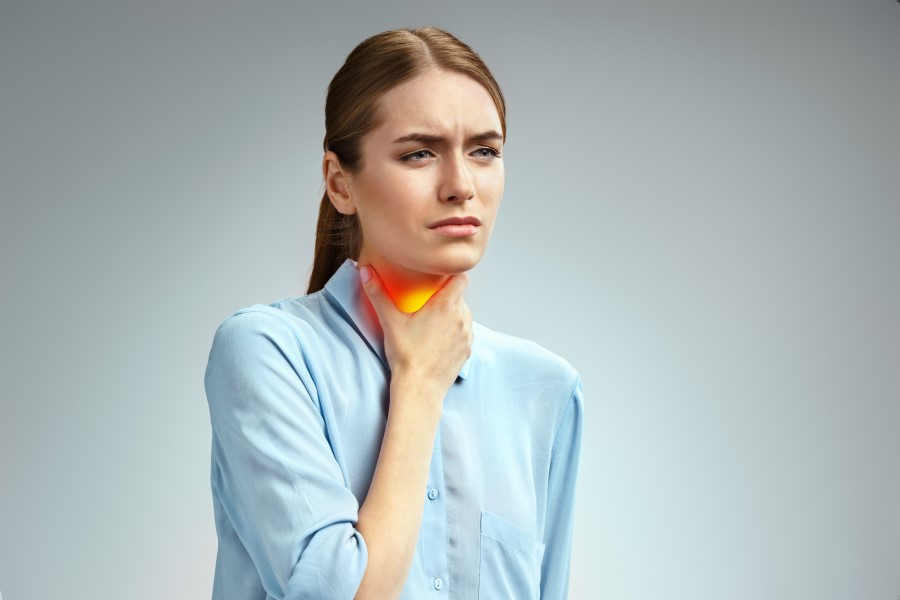 Kobieta trzyma się za szyję. Boli ją gardło z powodu anginy ropnej.