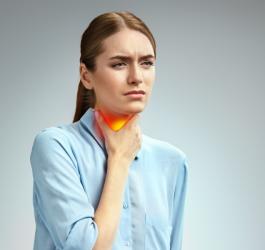 Kobieta trzyma się za szyję. Boli ją gardło z powodu anginy ropnej.