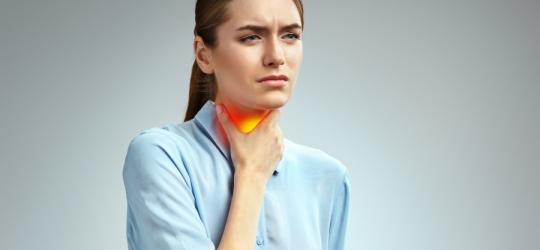 Kobieta trzyma się za szyję. Boli ją gardło z powodu anginy ropnej.