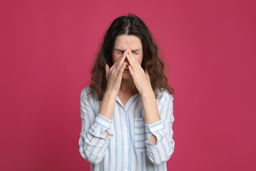 Kobieta trzyma się dłońmi za nos, dokucza jej zapalenie zatok.