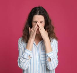 Kobieta trzyma się dłońmi za nos, dokucza jej zapalenie zatok.