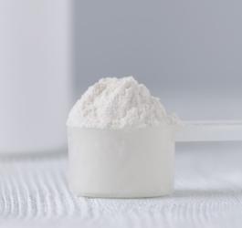 Plastikowa miarka wypełniona argininą w postaci proszku.