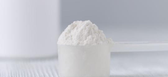 Plastikowa miarka wypełniona argininą w postaci proszku.