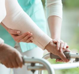 Starsza osoba przy wsparciu pielęgniarki korzysta z chodzika.