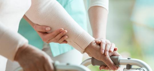 Starsza osoba przy wsparciu pielęgniarki korzysta z chodzika.