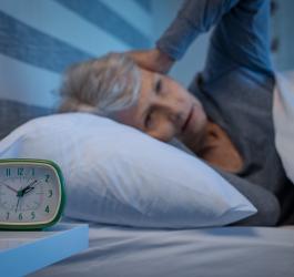 Starsza kobieta leży w łóżku, cierpi na bezsenność. Zegarek pokazuje godzinę 2 w nocy.