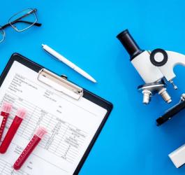 Mikroskop, okulary, kwestionariusz i próbki krwi w fiolkach na niebieskim tle.