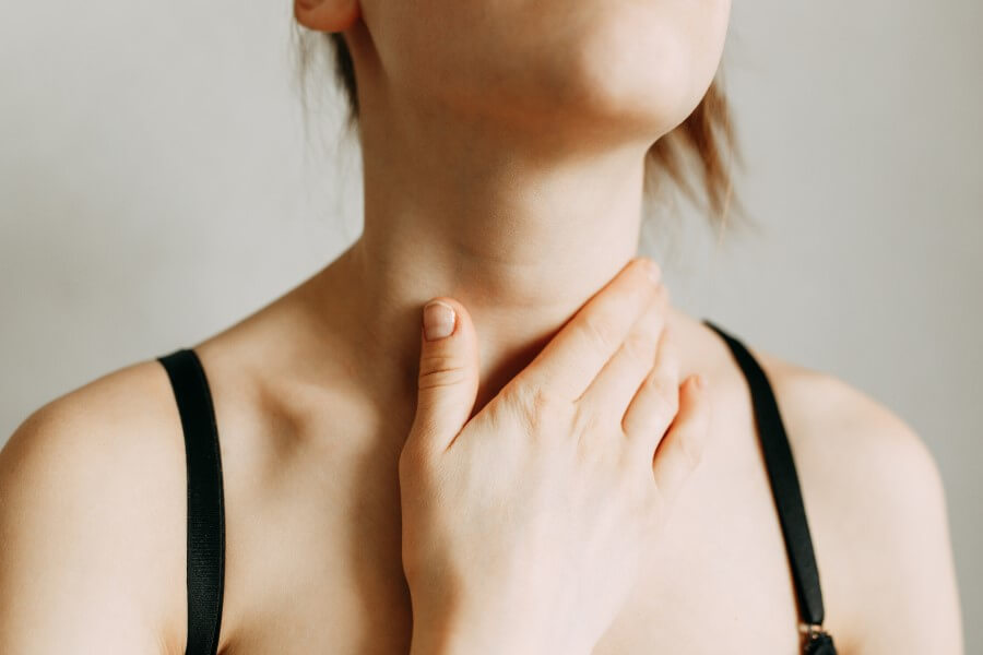 Kobieta chwyta się za szyję w okolicy tarczycy.