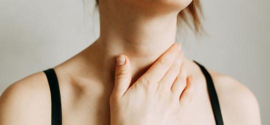 Kobieta chwyta się za szyję w okolicy tarczycy.