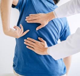 Pacjent u lekarza, który skarży się na ból mięśni pleców i wskazuje, gdzie odczuwa ból.