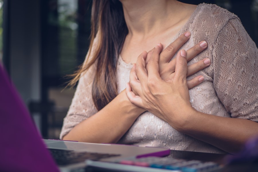 Kobieta chwyta się za klatkę piersiową, odczuwa ból piersi.