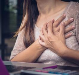 Kobieta chwyta się za klatkę piersiową, odczuwa ból piersi.