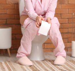 Kobieta siedzi na toalecie, odczuwa ból przy oddawaniu moczu.