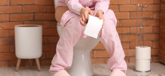 Kobieta siedzi na toalecie, odczuwa ból przy oddawaniu moczu.