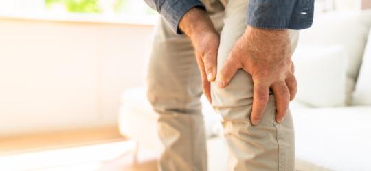 Mężczyzna chwyta się za nogę, odczuwa ból stawu kolanowego.
