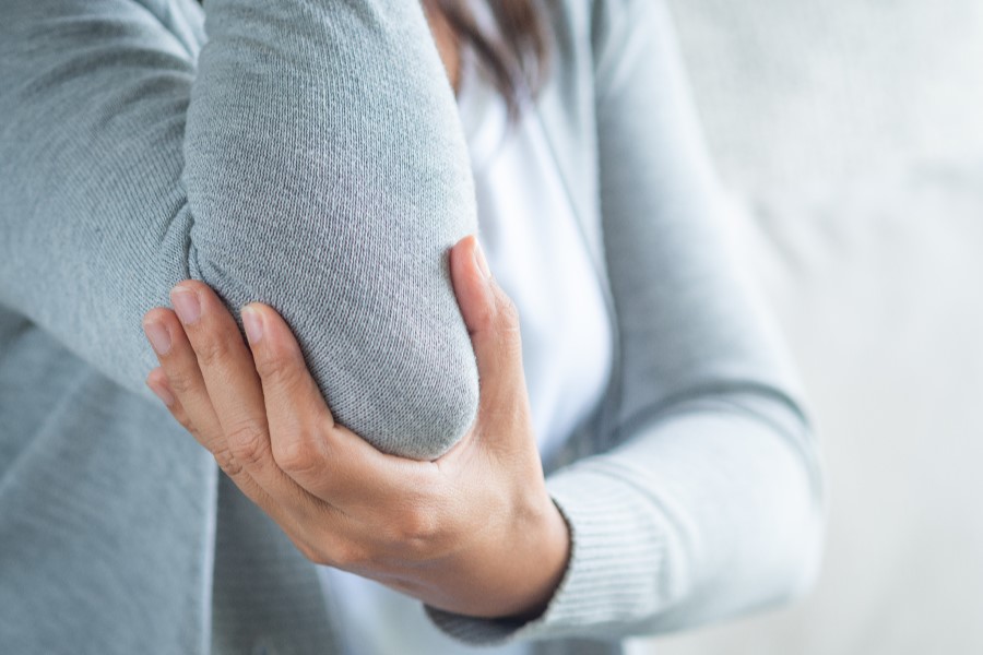 Kobieta trzyma się za łokieć. Odczuwa ból w łokciu.