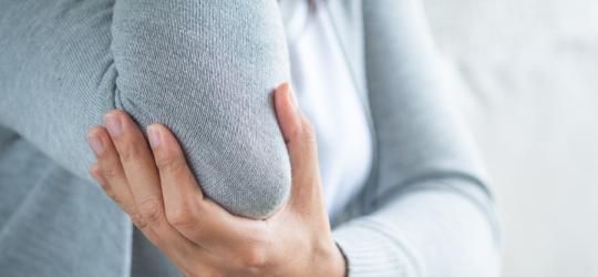 Kobieta trzyma się za łokieć. Odczuwa ból w łokciu.