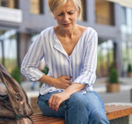 Kobieta w średnim wieku, siedzi na ławce. Trzyma się za brzuch, bo męczy ją ból żołądka.