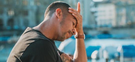 Mężczyzna przykłada dłoń do czoła. Boli go głowa.