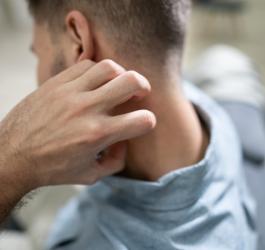 Mężczyzna drapie się po karku, dokuczają mu brodawczaki na szyi.