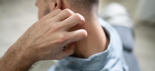 Mężczyzna drapie się po karku, dokuczają mu brodawczaki na szyi.