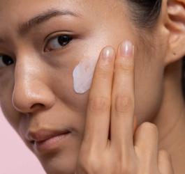 Kobieta rozsmarowuje dłonią krem na policzku.