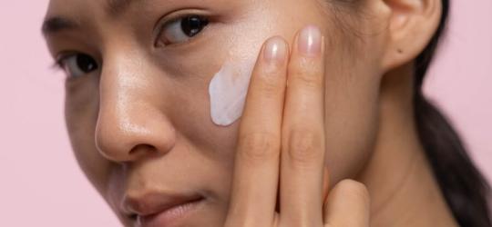 Kobieta rozsmarowuje dłonią krem na policzku.