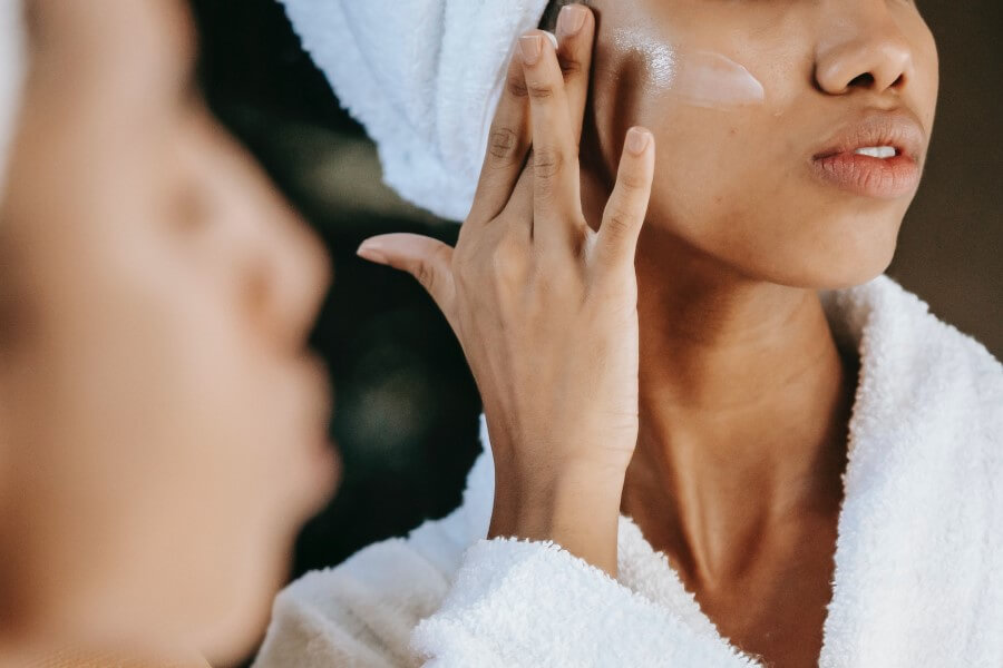 Kobieta po kąpieli przeprowadza pielęgnację skóry twarzy.