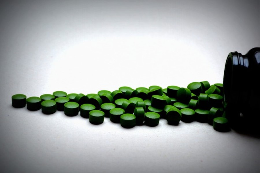 Zielone tabletki chlorelli wysypane z butelki.