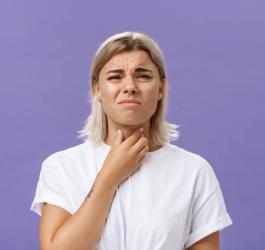 Młoda kobieta chwyta się za gardło, dokucza jej chrypka.