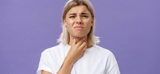 Młoda kobieta chwyta się za gardło, dokucza jej chrypka.