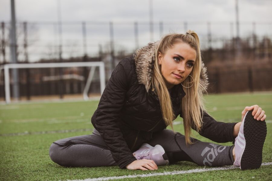 Młoda kobieta w sportowym stroju, na boisku. Rozciąga się po treningu.