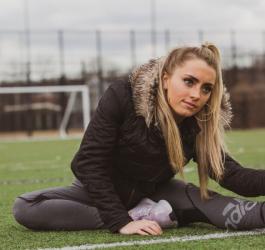 Młoda kobieta w sportowym stroju, na boisku. Rozciąga się po treningu.