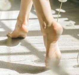 Zbliżenie na kobiece, bose stopy idące po betonowej posadzce.