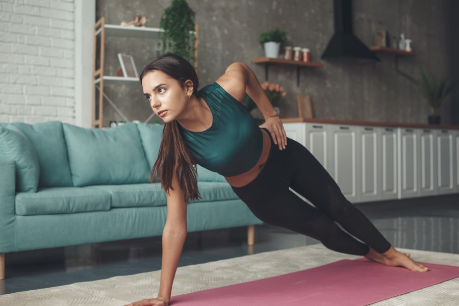 Kobieta ćwiczy w mieszkaniu, wykonuje na macie ćwiczenia izometryczne.