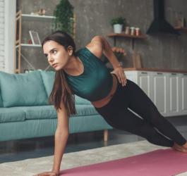 Kobieta ćwiczy w mieszkaniu, wykonuje na macie ćwiczenia izometryczne.