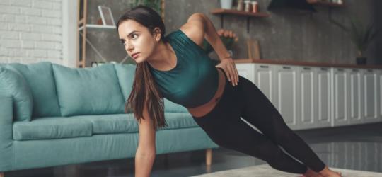 Kobieta ćwiczy w mieszkaniu, wykonuje na macie ćwiczenia izometryczne.