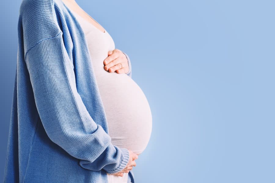 Ciężarna kobieta trzyma się za ciążowy brzuszek.