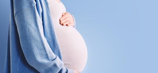 Ciężarna kobieta trzyma się za ciążowy brzuszek.