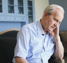 Starszy, zmartwiony mężczyzna siedzi na fotelu. Zmaga się z postępującą demencją starczą.