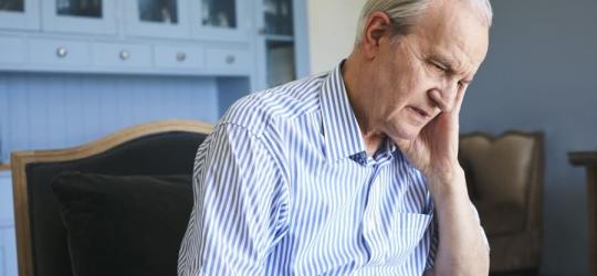 Starszy, zmartwiony mężczyzna siedzi na fotelu. Zmaga się z postępującą demencją starczą.