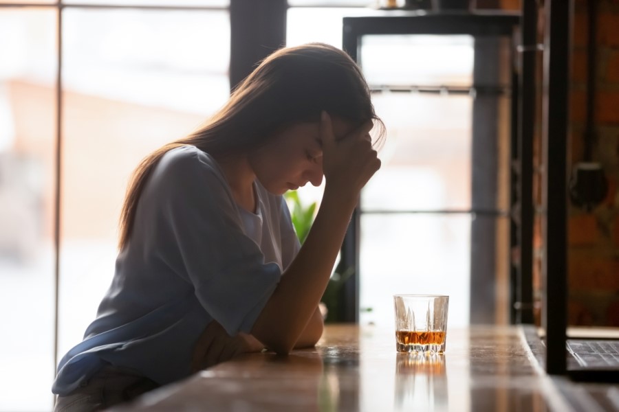Kobieta siedzi przy barze przy szklance alkoholu.
