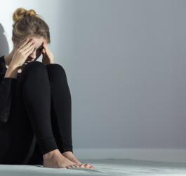 Kobieta siedzi na ziemi, oparta o ścianę, jest zdenerwowana i smutna.