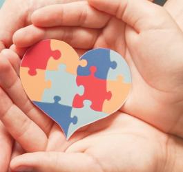 Ręce dziecka trzymane przez ręce rodzica. W złączonych dłoniach widoczne serce z puzzli.