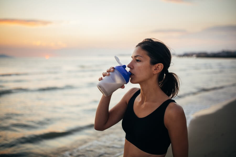 Kobieta w stroju sportowym na plaży. Nawadnia się po treningu.