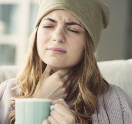 Kobiecie doskwiera flegma w gardle, trzyma się dłonią za szyję.