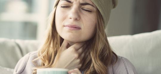 Kobiecie doskwiera flegma w gardle, trzyma się dłonią za szyję.